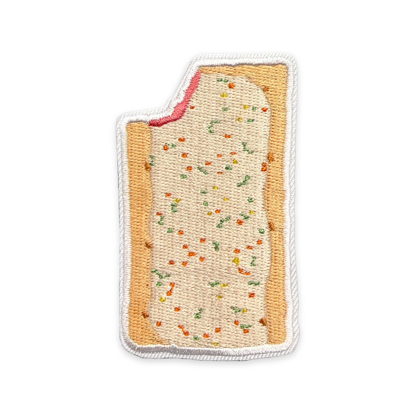An embroidered patch shaped like a slice of toast or a pastry, with a beige filling, orange-brown edges, small multicolored confetti-like details, and a white stitched border on a plain white background.