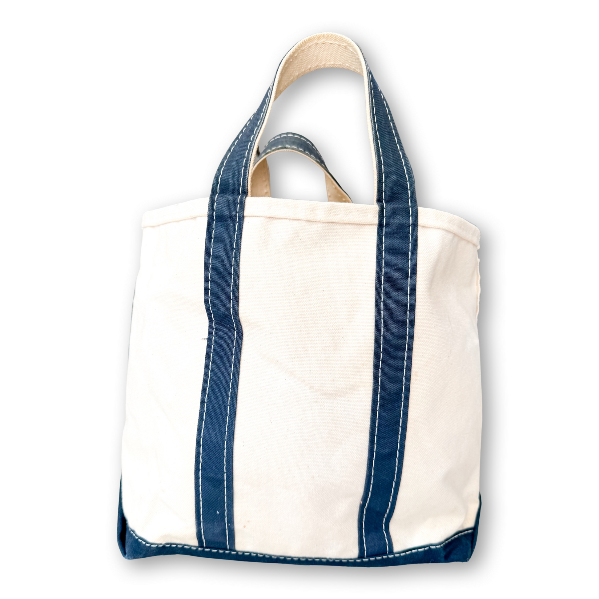 A canvas tote bag with off-white body panels and dark navy blue trim, featuring double top handles and white contrast stitching, shown against a plain white background.