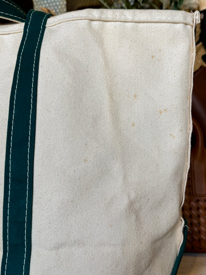 Close-up of a beige tote bag with green straps on a blurred background