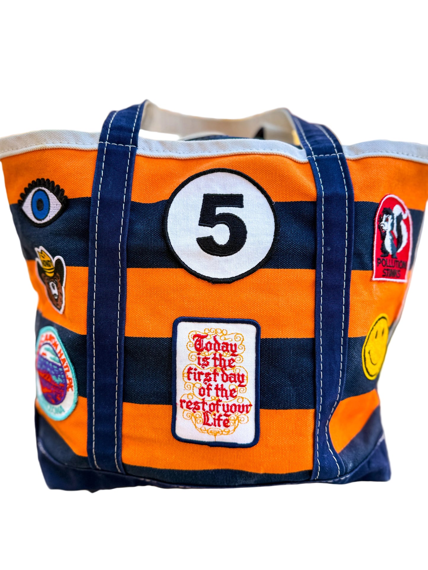 Orange and navy tote bag with patches and text, outdoors.