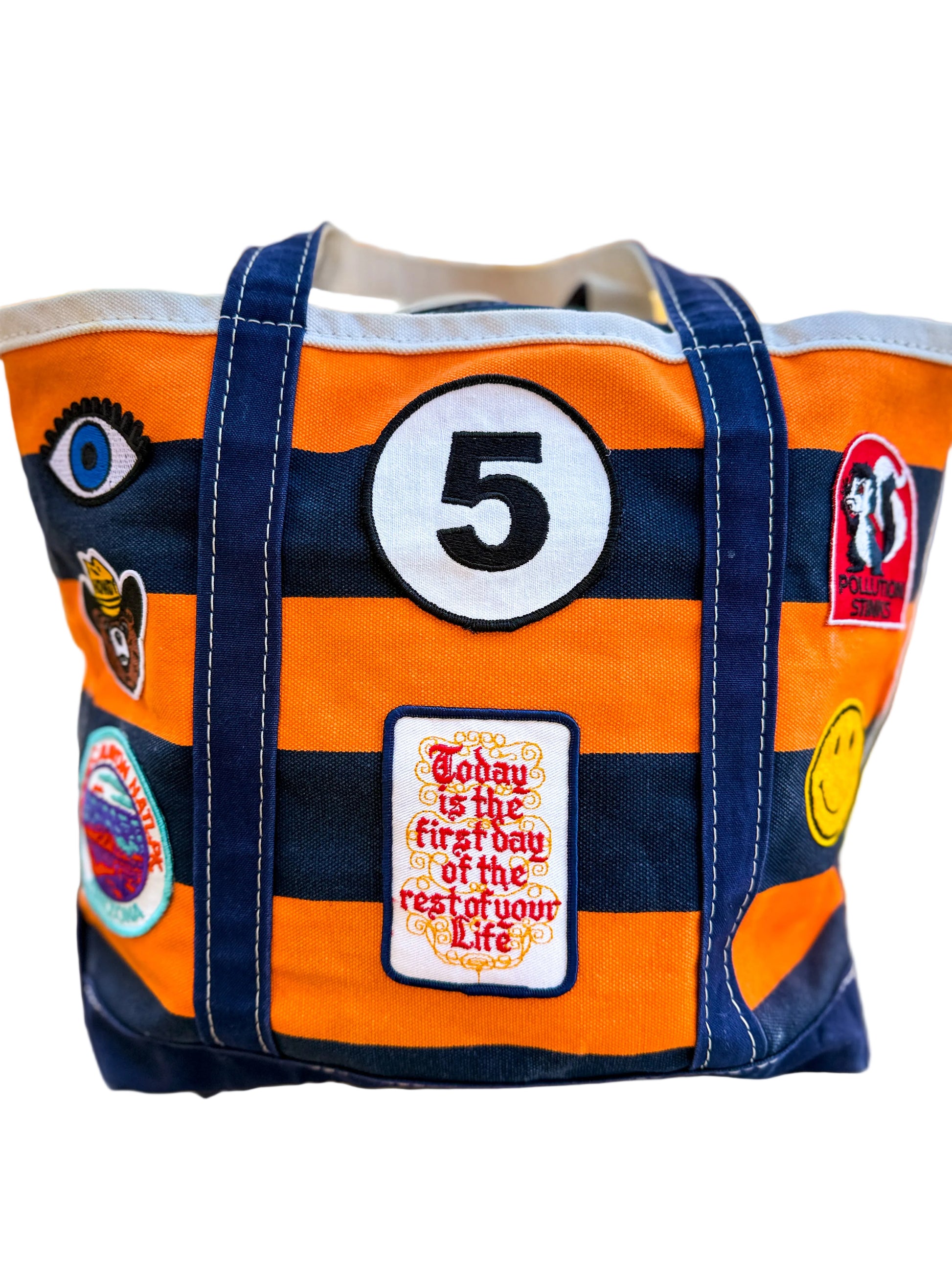 Orange and navy tote bag with patches and text, outdoors.