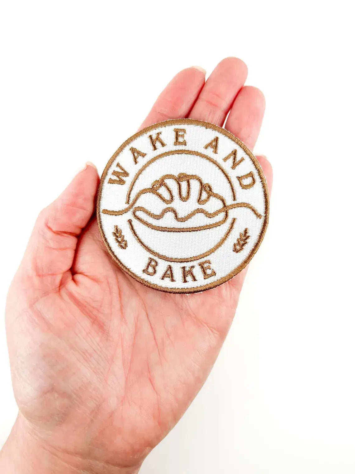 Hand holding a 'Wake and Bake' patch with a white background