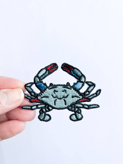 Hand holding a crab-shaped patch against a white background