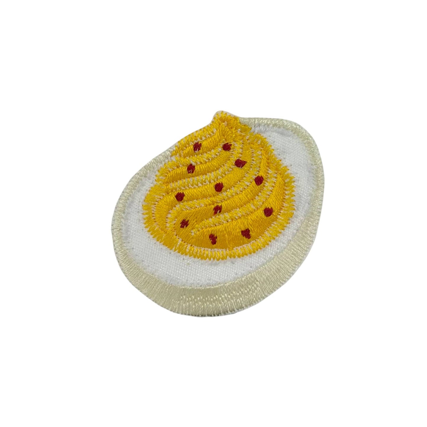 Embroidered patch of a deviled egg with a yellow yolk and red spots on a white background