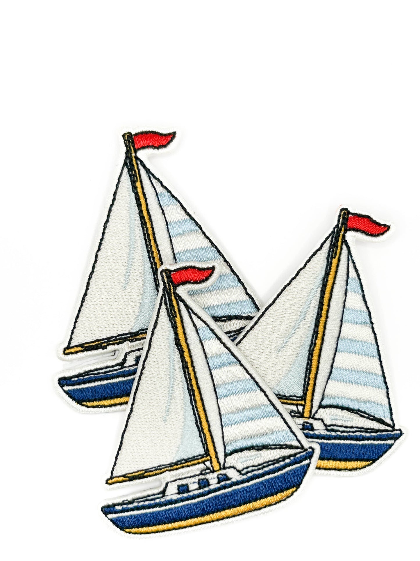 Three embroidered sailboats with striped sails and red flags on a white background