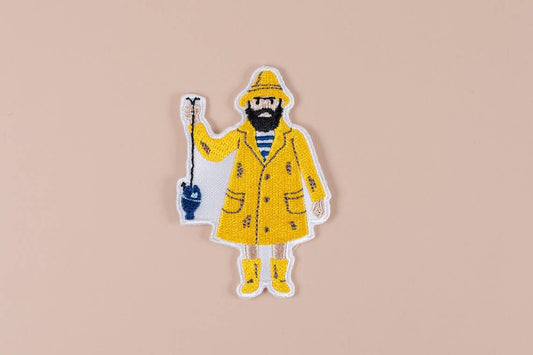 Sticker of a fisherman wearing a yellow raincoat and boots holding a fishing line with a blue fish attached on a beige background