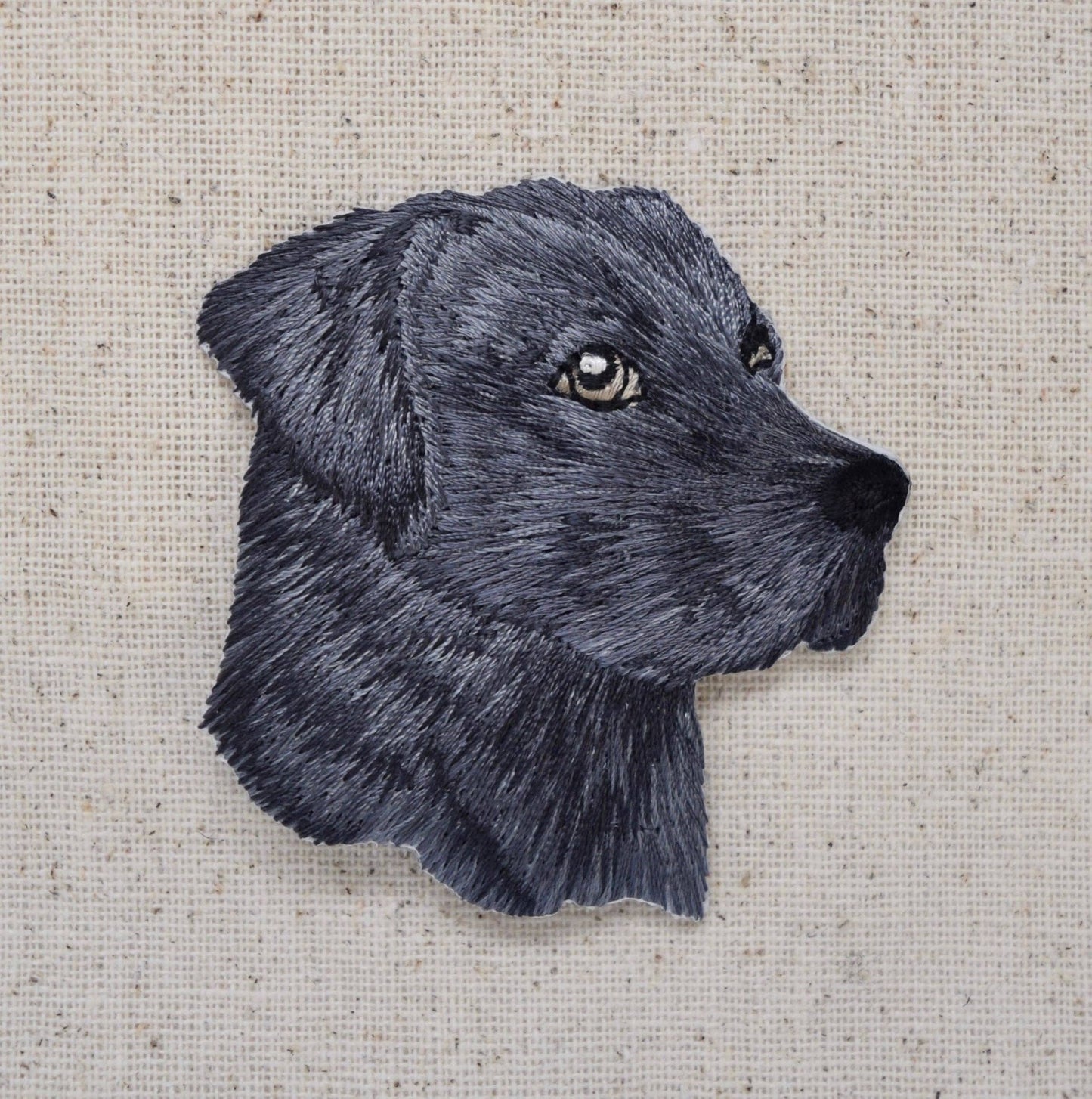 Embroidered black dog's head on a textured beige background