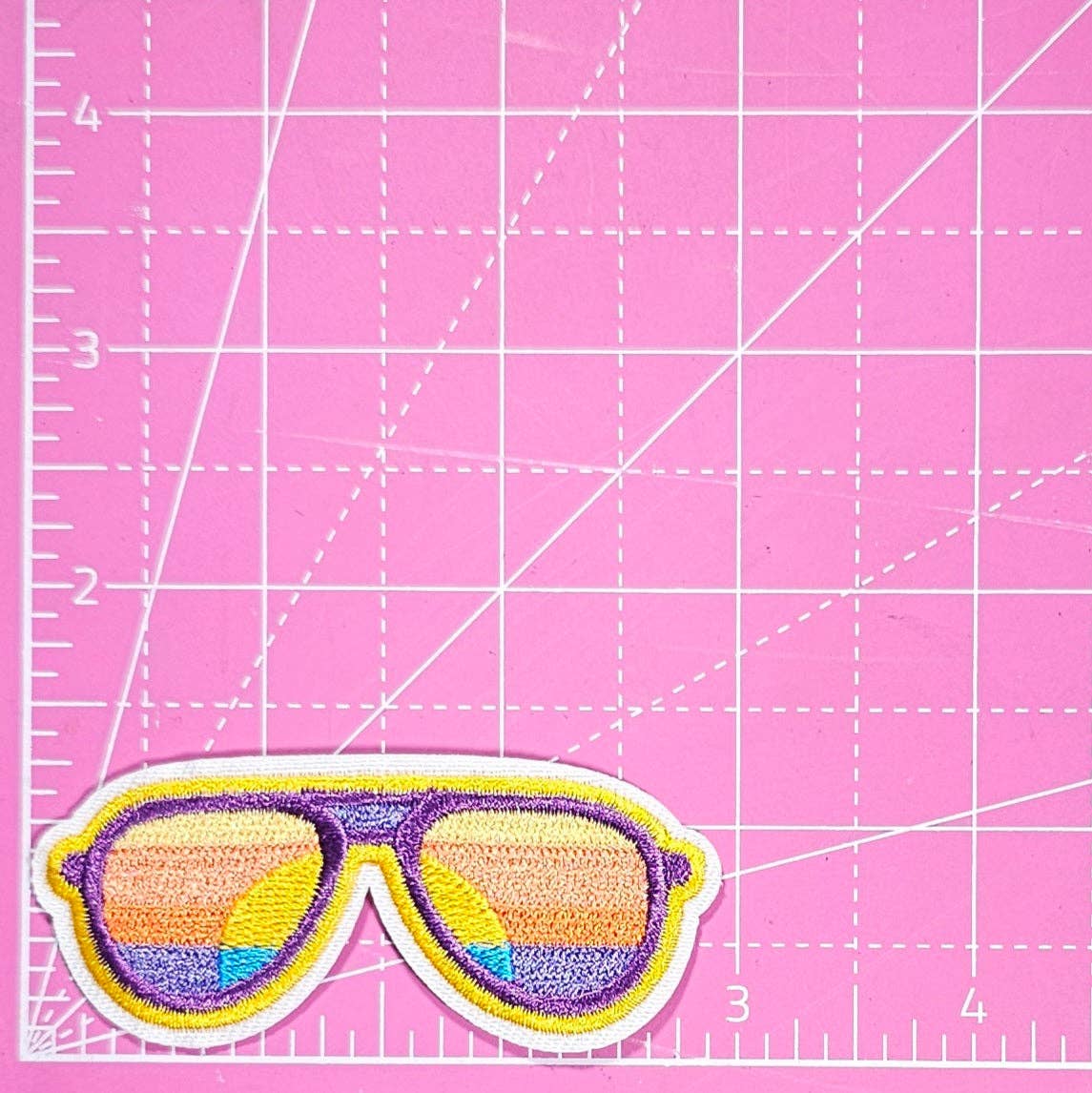 Sunglasses patch on a pink cutting mat with grid lines