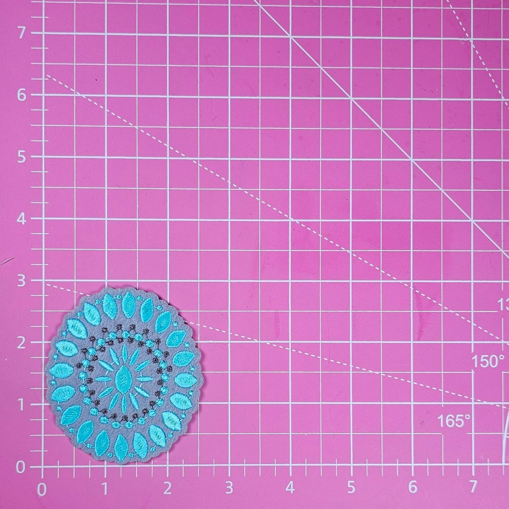 Blue mandala patch on a pink cutting mat with grid lines