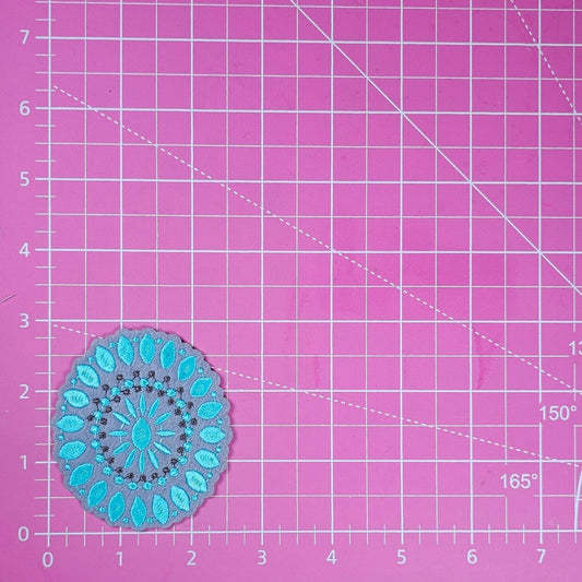 Blue mandala patch on a pink cutting mat with grid lines