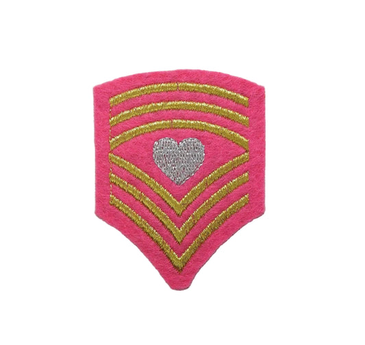Pink military rank insignia shield patch with gold stripes and a heart emblem on a textured beige background