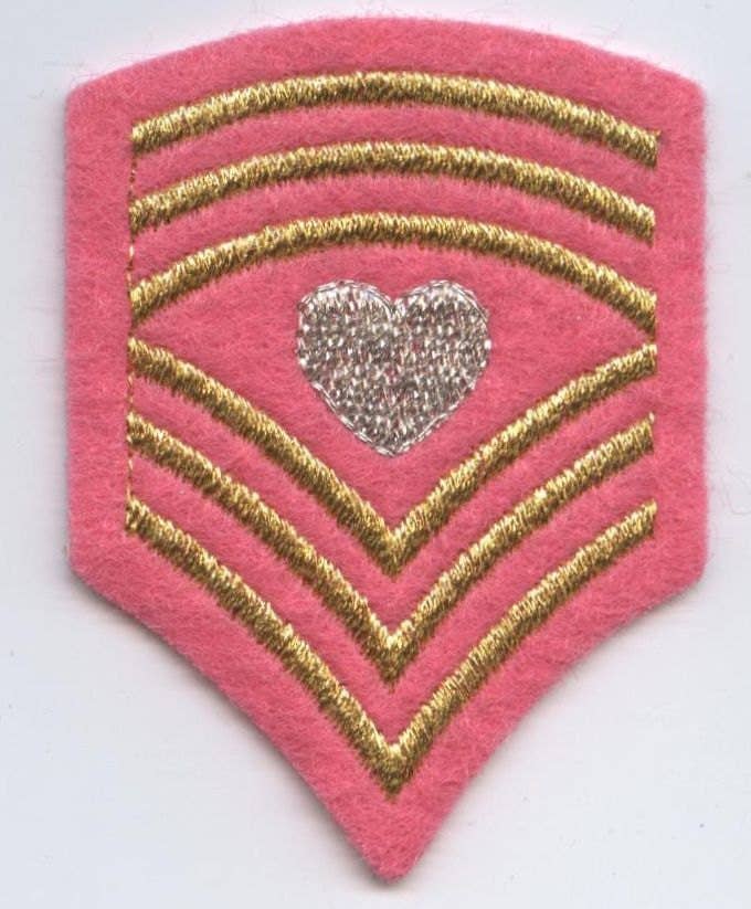 Pink shield patch with gold stripes and a silver heart in the center on a white background