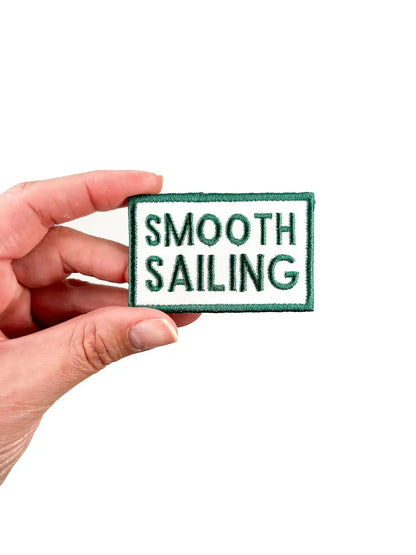 Hand holding a patch with 'Smooth Sailing' text on a white background