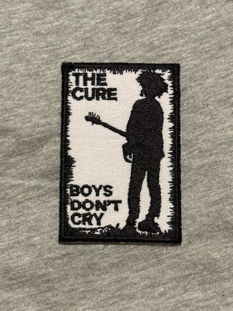 Patch with 'The Cure' design featuring a silhouette of a person holding a guitar and 'Boys Don't Cry' text on a gray background.