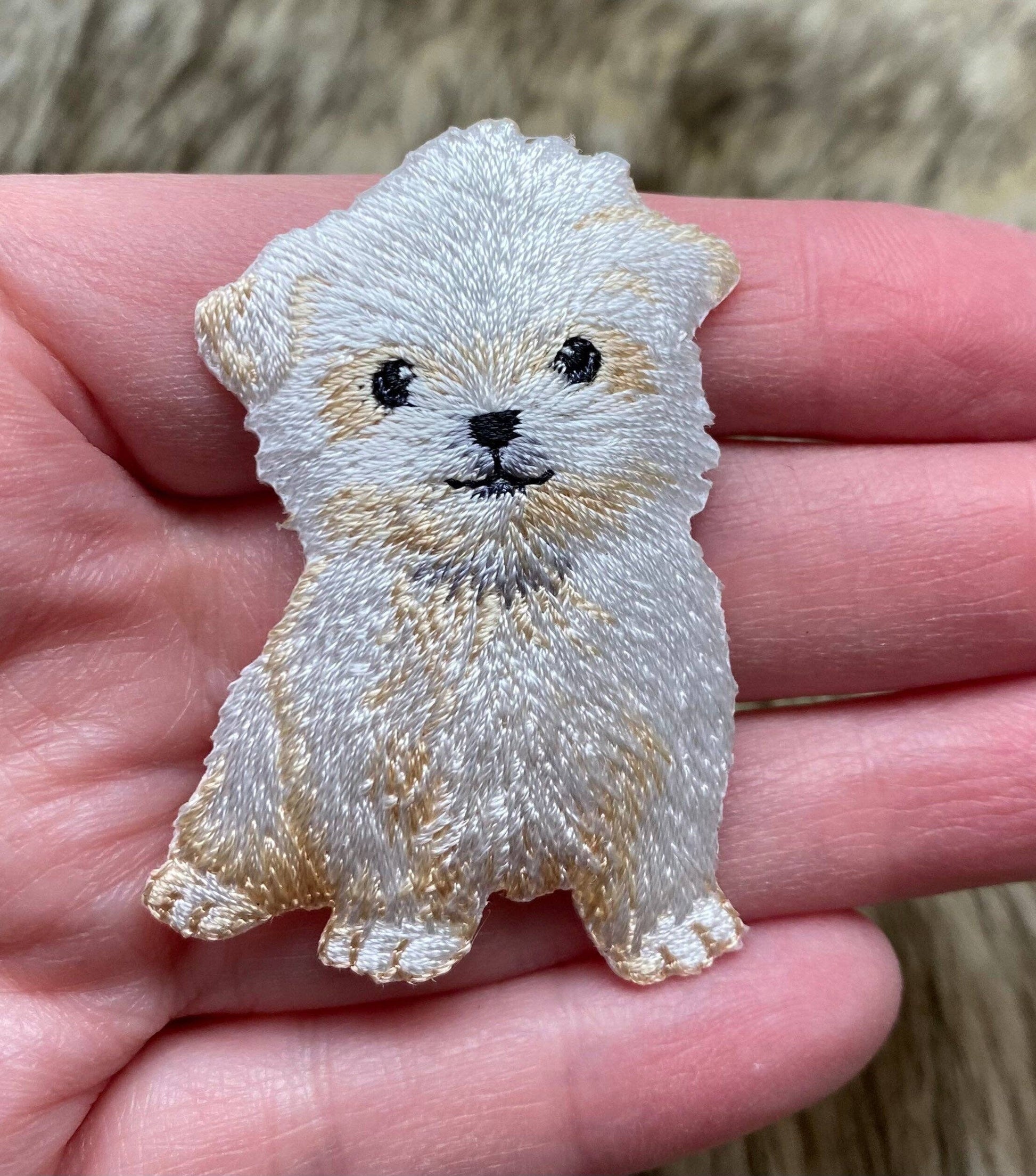 Embroidered patch of a dog held in a hand with a blurred natural background