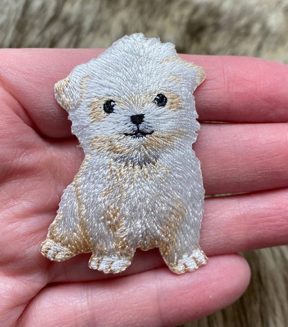 Embroidered patch of a dog held in a hand with a blurred natural background