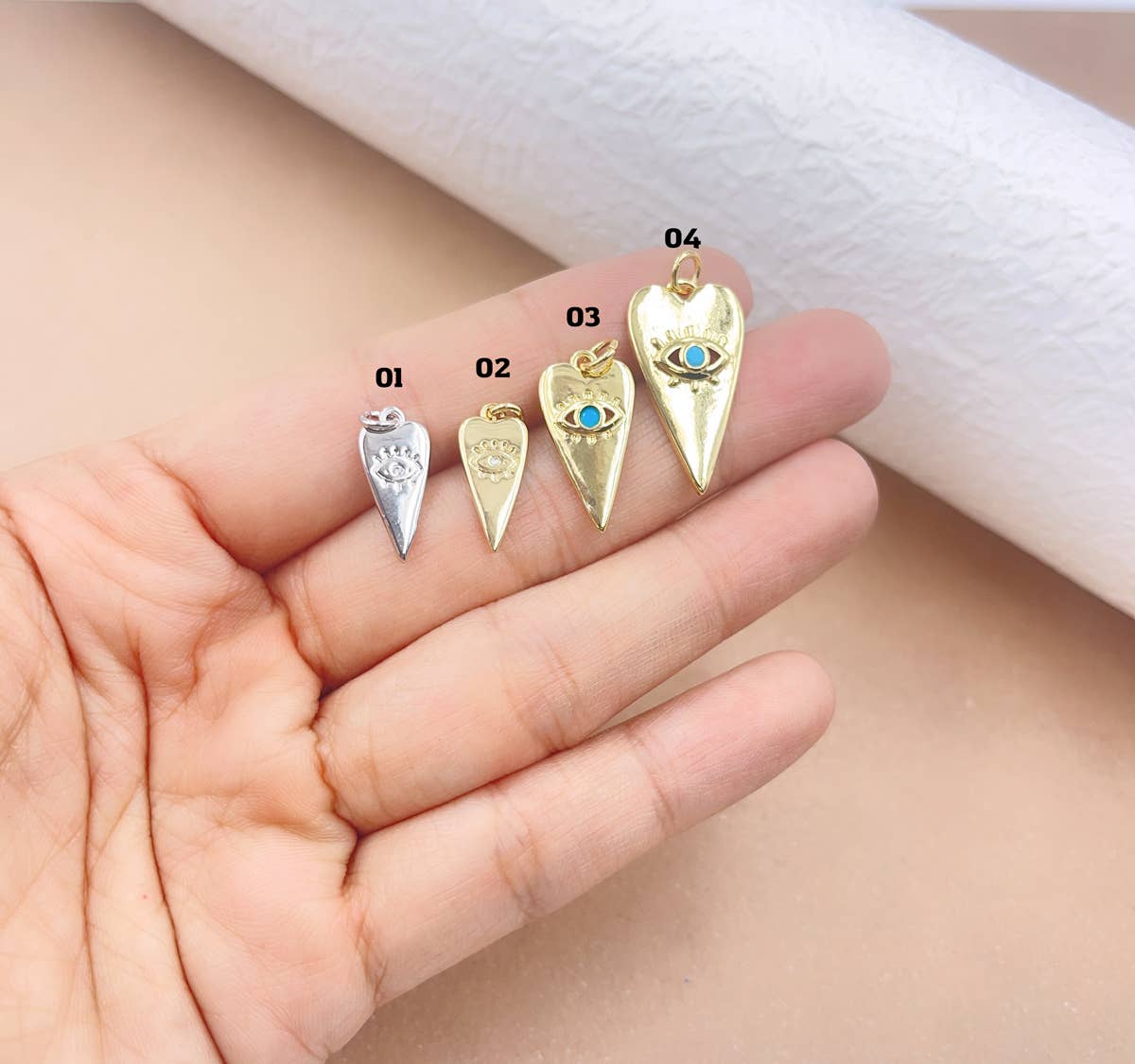 Four gold evil eye heart pendants on a hand with a white cloth background