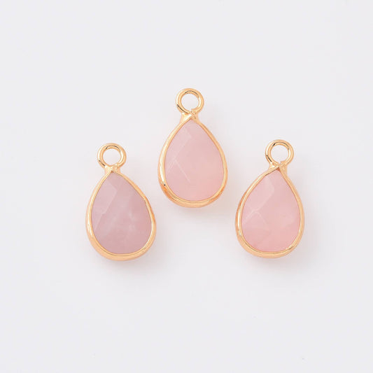 Three pink teardrop-shaped rose quartz charms with gold frames on a white background