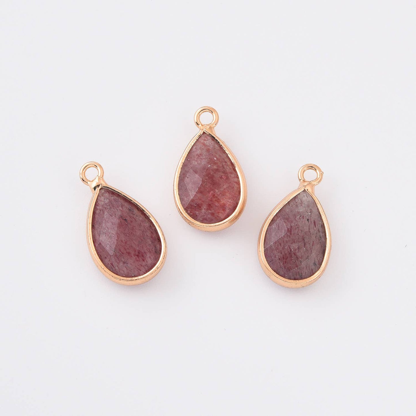 Three teardrop-shaped strawberry quartz gemstones in gold settings on a white background