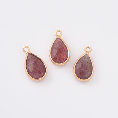 Three teardrop-shaped strawberry quartz gemstones in gold settings on a white background