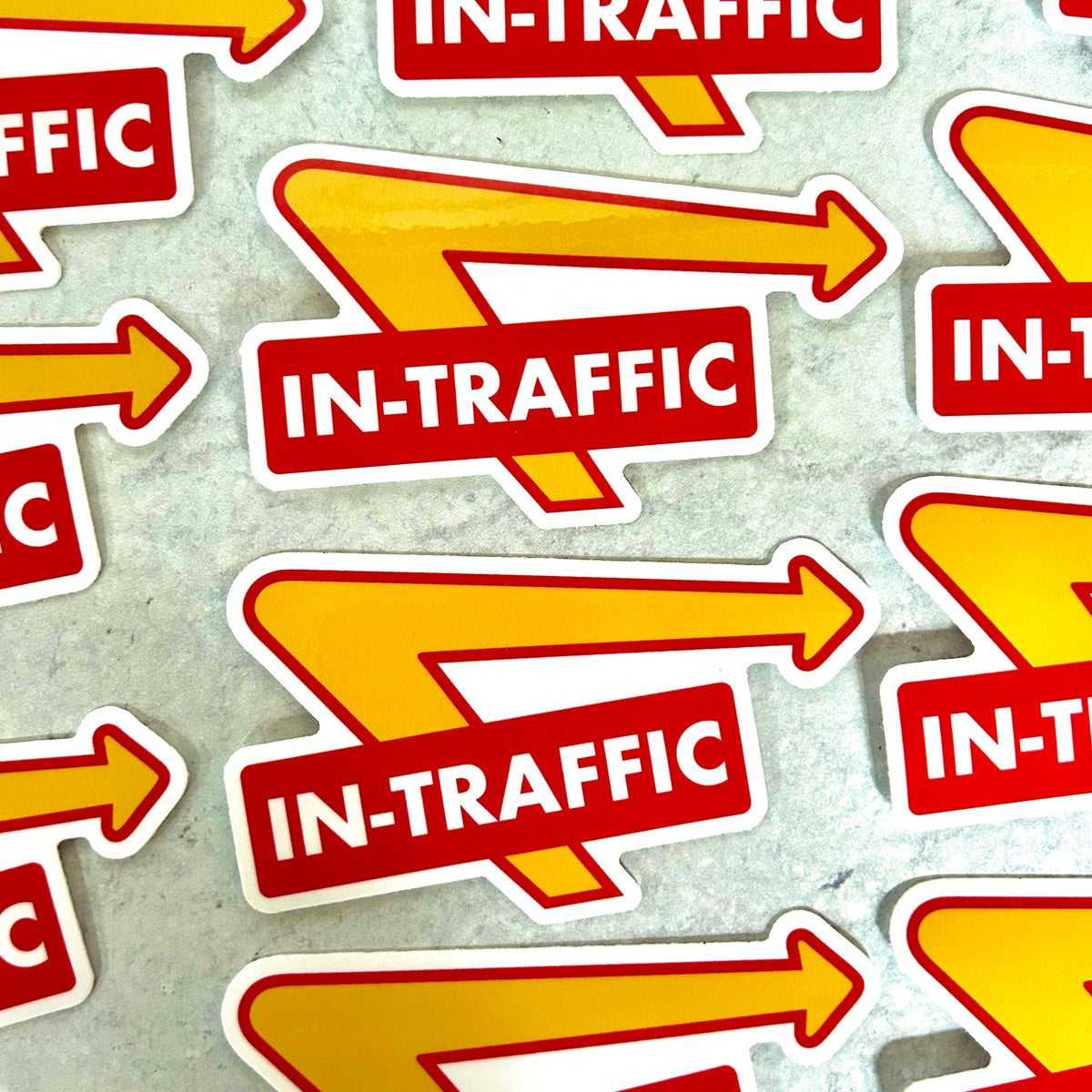 Multiple die-cut stickers featuring a red and yellow 'IN-TRAFFIC' arrow design, arranged on a light gray textured surface.