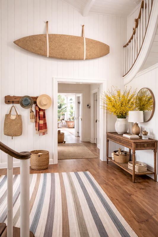 coastal-themed hallway with a surfboard, striped rug, and decorative items.