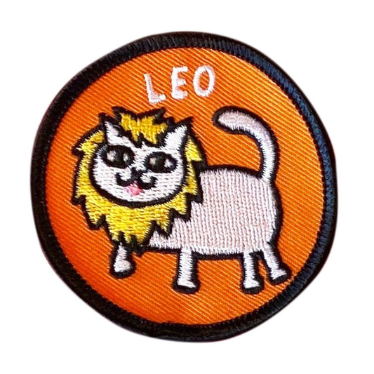 A circular embroidered patch featuring a cartoon lion cat with a white body, yellow mane, and black outlines on an orange background, with the word 'LEO' stitched at the top.