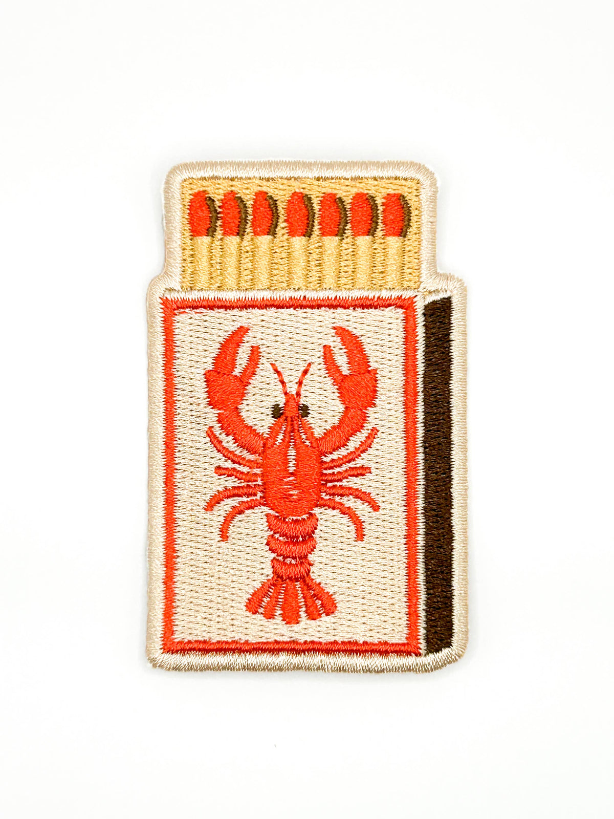An embroidered patch shaped like a matchbox, featuring a red lobster design on the front, red matches at the top, and a dark brown side edge, shown on a plain white background.