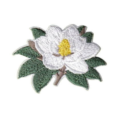 An embroidered magnolia flower patch with white petals, a yellow center, and green leaves on a brown stem, shown on a plain white background.