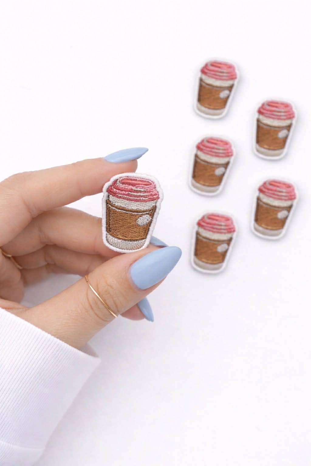 Hand holding coffee cup-shaped earrings with a white background