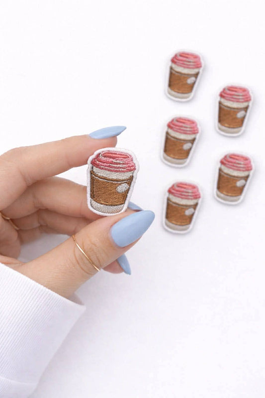 Hand holding coffee cup-shaped earrings with a white background