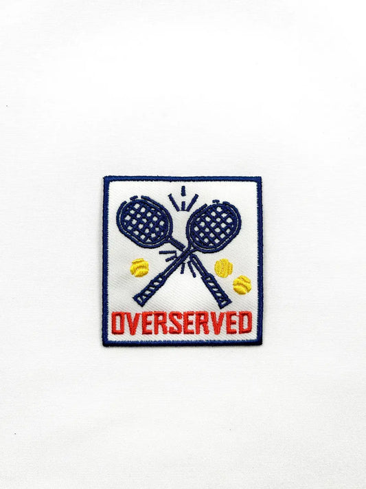Embroidered patch with tennis rackets and balls and the word 'Overserved' on a white background.