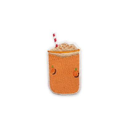 An embroidered patch shaped like a pumpkin spice latte, featuring a textured orange body, a white foam top, a red and white striped straw, and small embroidered orange pumpkins on the front, set against a plain white background.