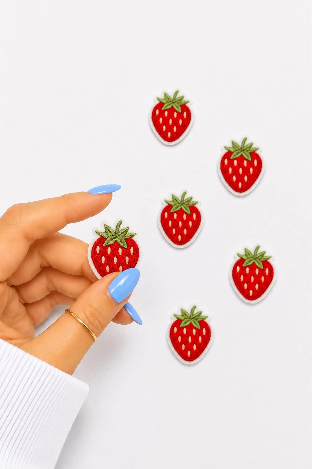 Strawberry-shaped earrings on a white background with a hand holding one earring.