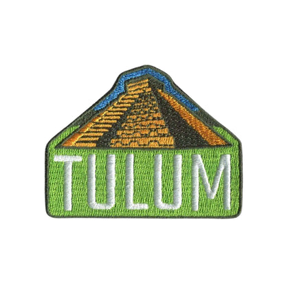 An embroidered patch featuring a green house-shaped border with the word 'TULUM' in white letters across the bottom and a pyramid design in gold, black, and blue above, shown on a plain white background.